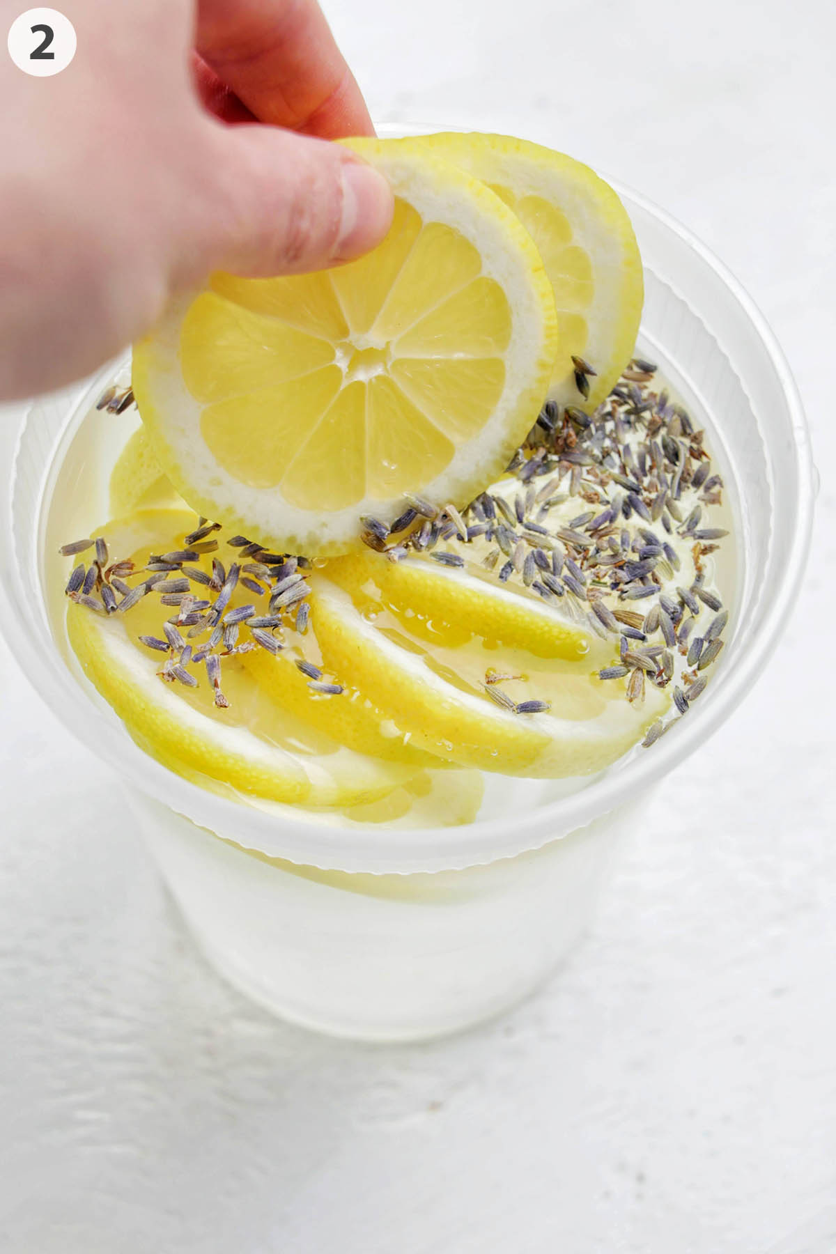 numbered photo showing a hand placing lemons into a container with vodka and lavender.