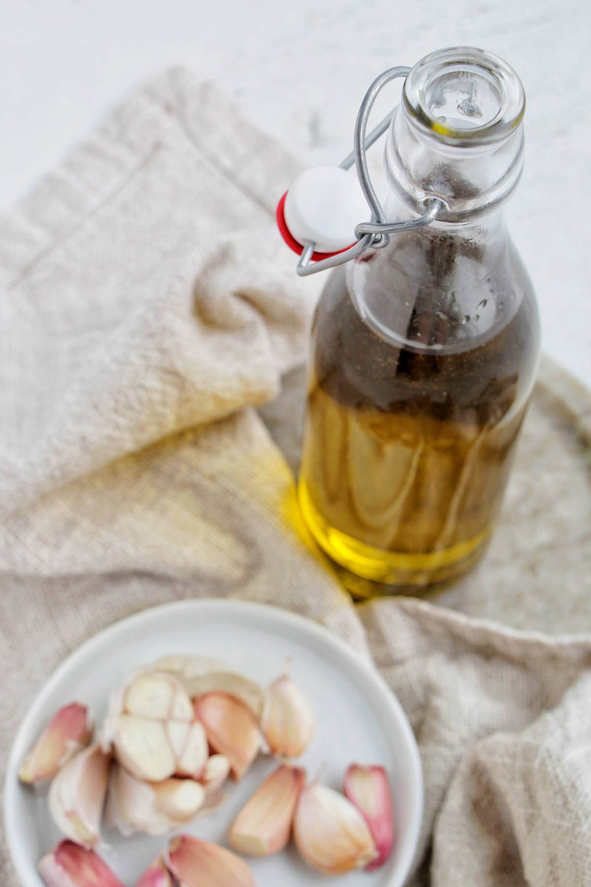garlic infused olive oil in a glass jar next to a plate of garlic cloves.