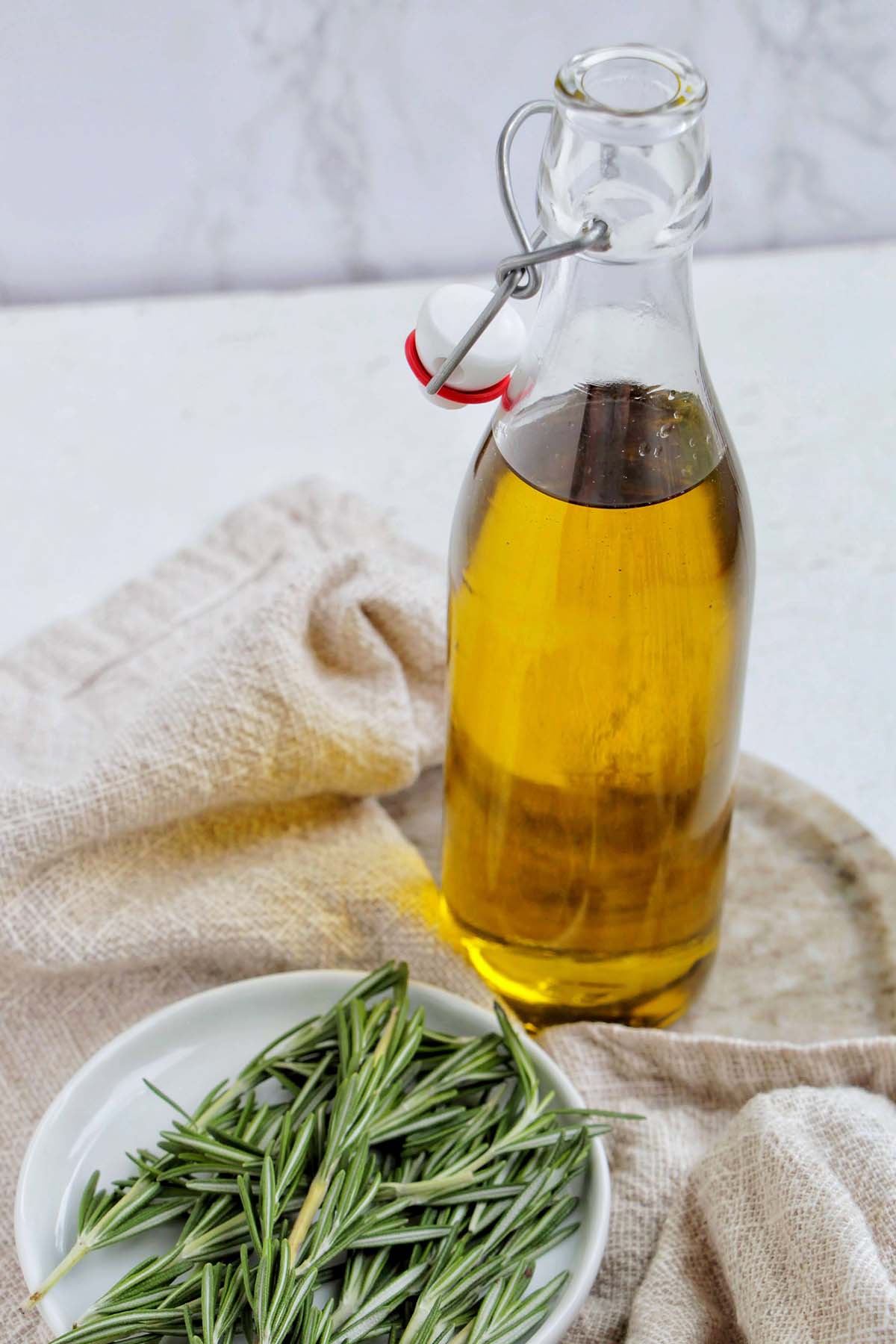 rosemary infused olive oil in a glass jar next to a plate of rosemary.