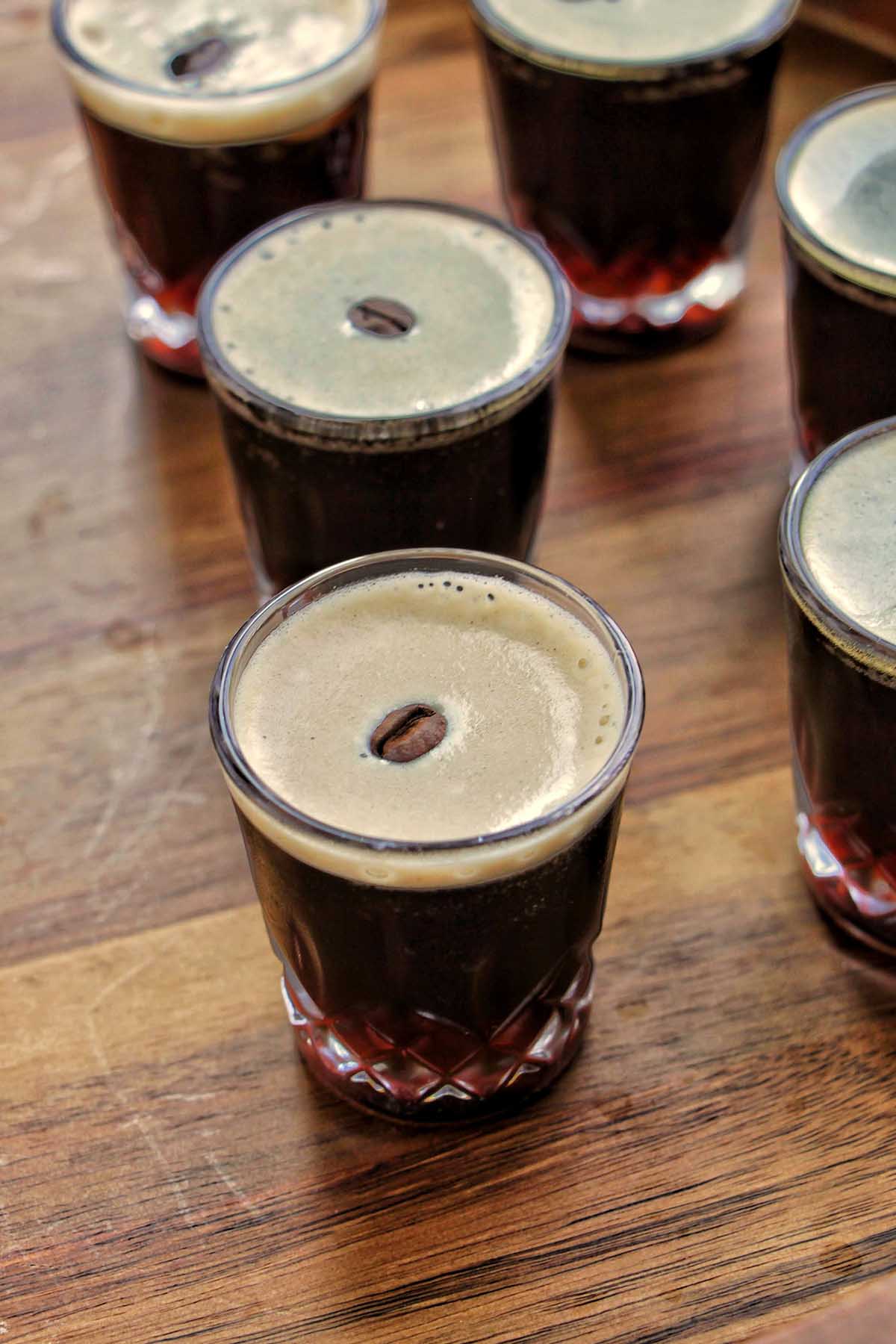 espresso martini shots on a wooden serving tray.