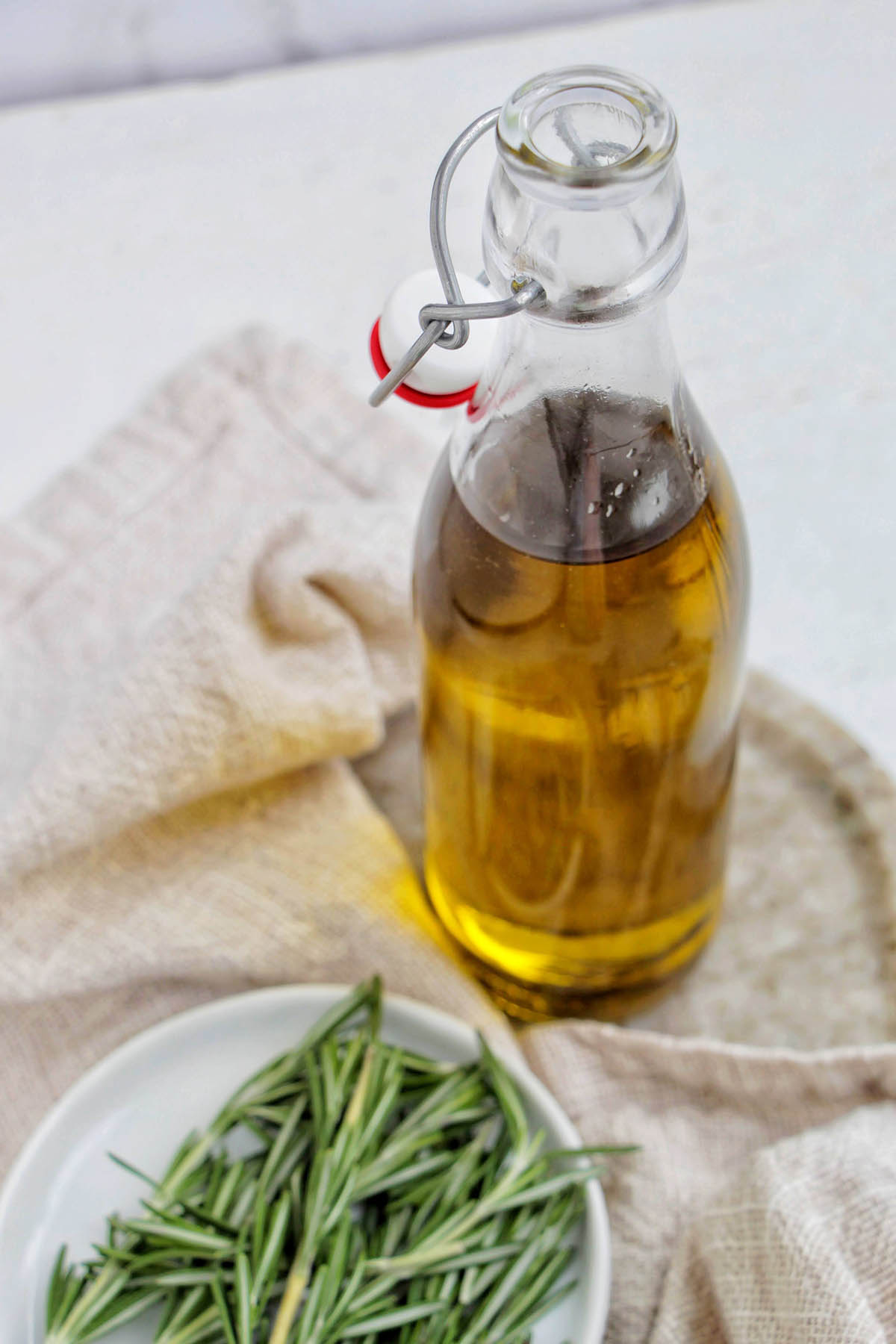rosemary olive oil in a glass jar next to a plate of rosemary.
