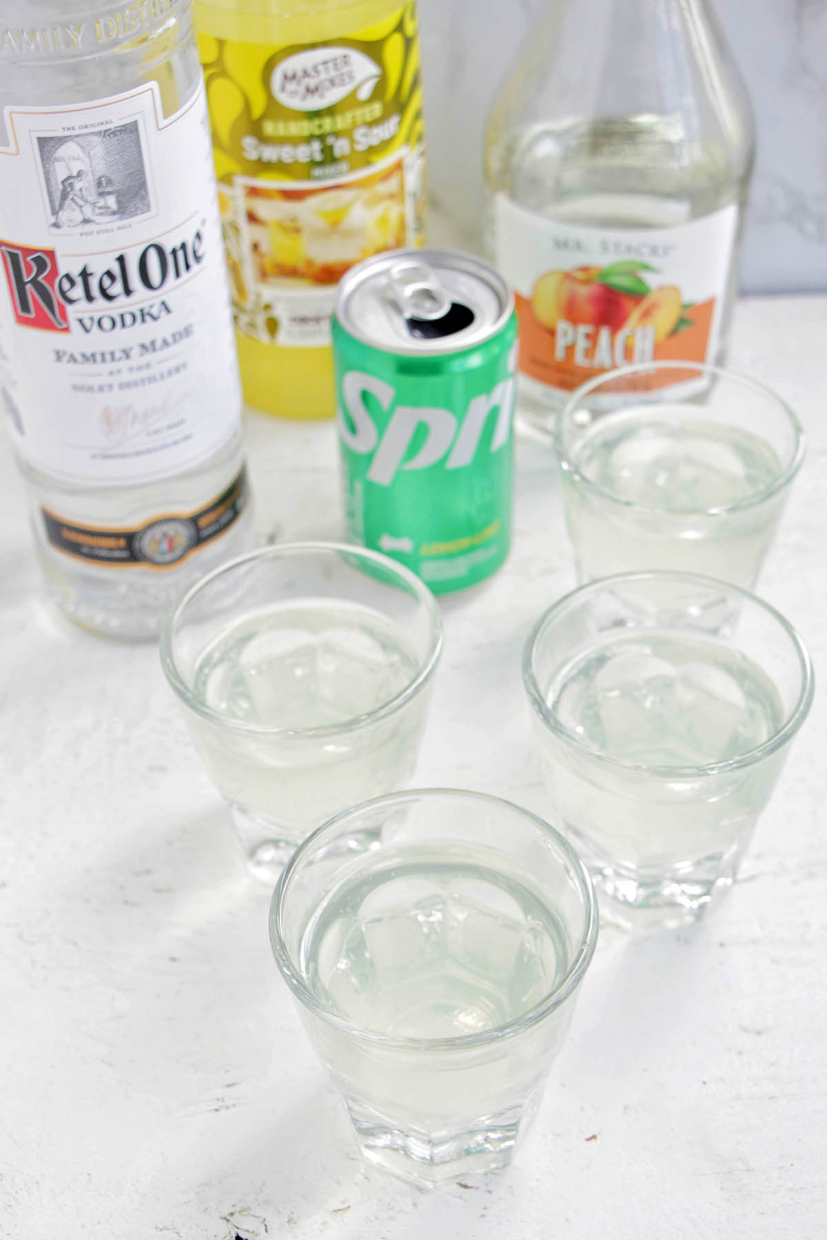four white tea shots in rocks glasses next to alcohol bottles.