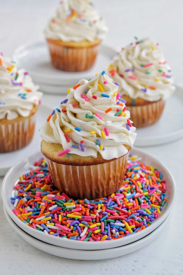 four cupcakes with vanilla frosting sitting on small plates.