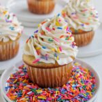 four cupcakes with vanilla frosting sitting on small plates.