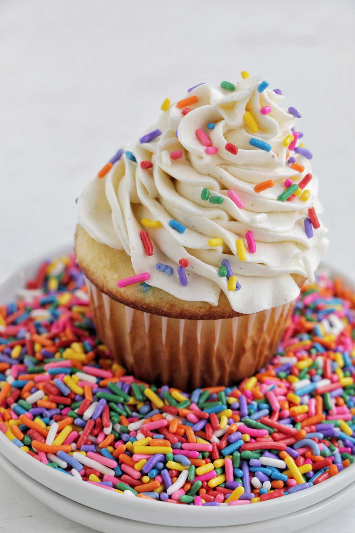 cupcake with vanilla frosting sitting on a plate of sprinkles.