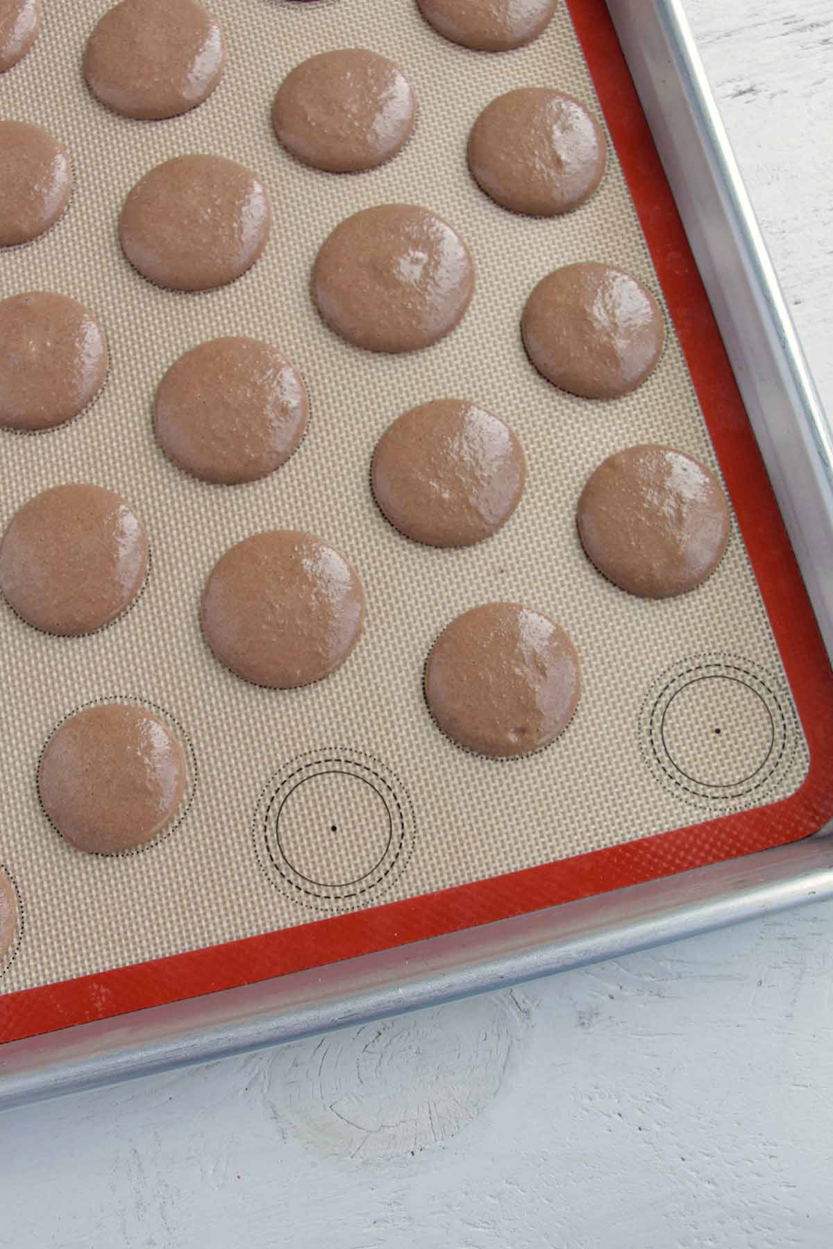 chocolate macarons piped onto a parchment mat.