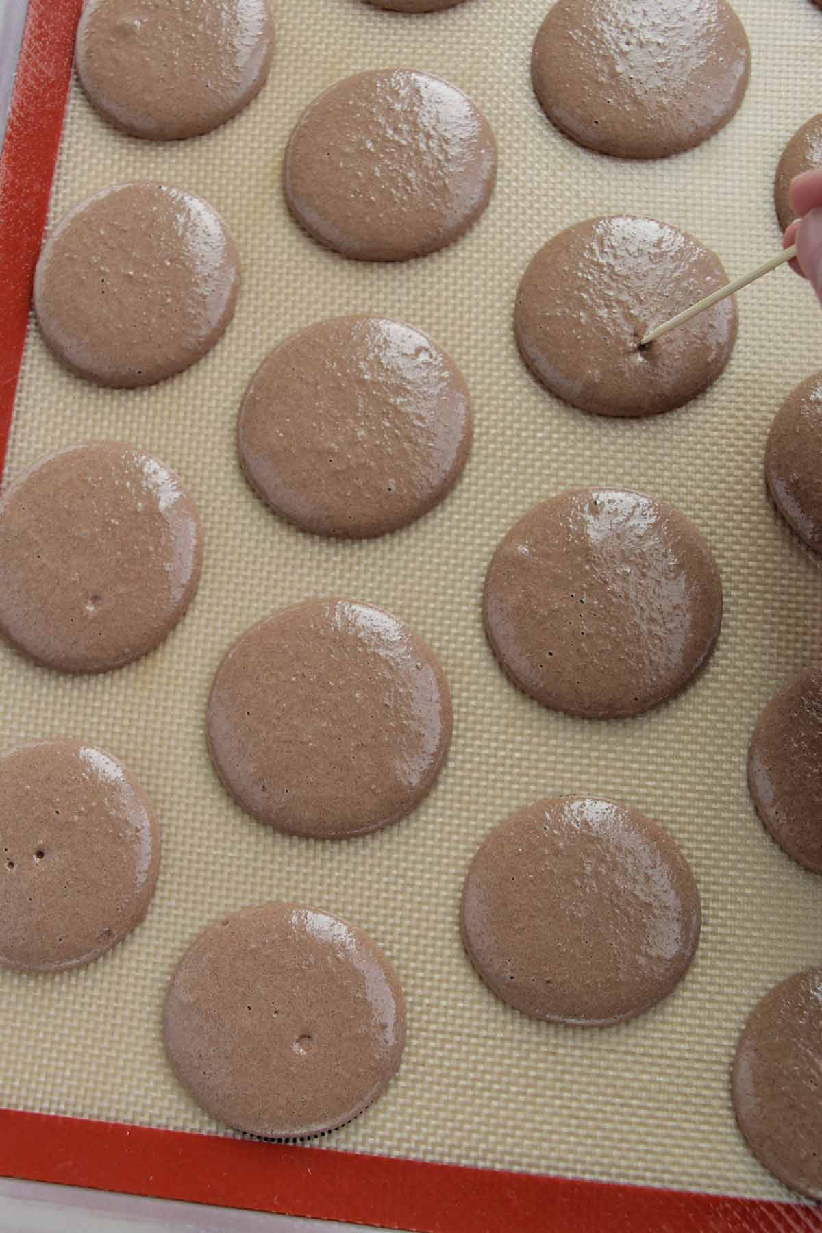 popping chocolate macaron air bubbles with a toothpick.