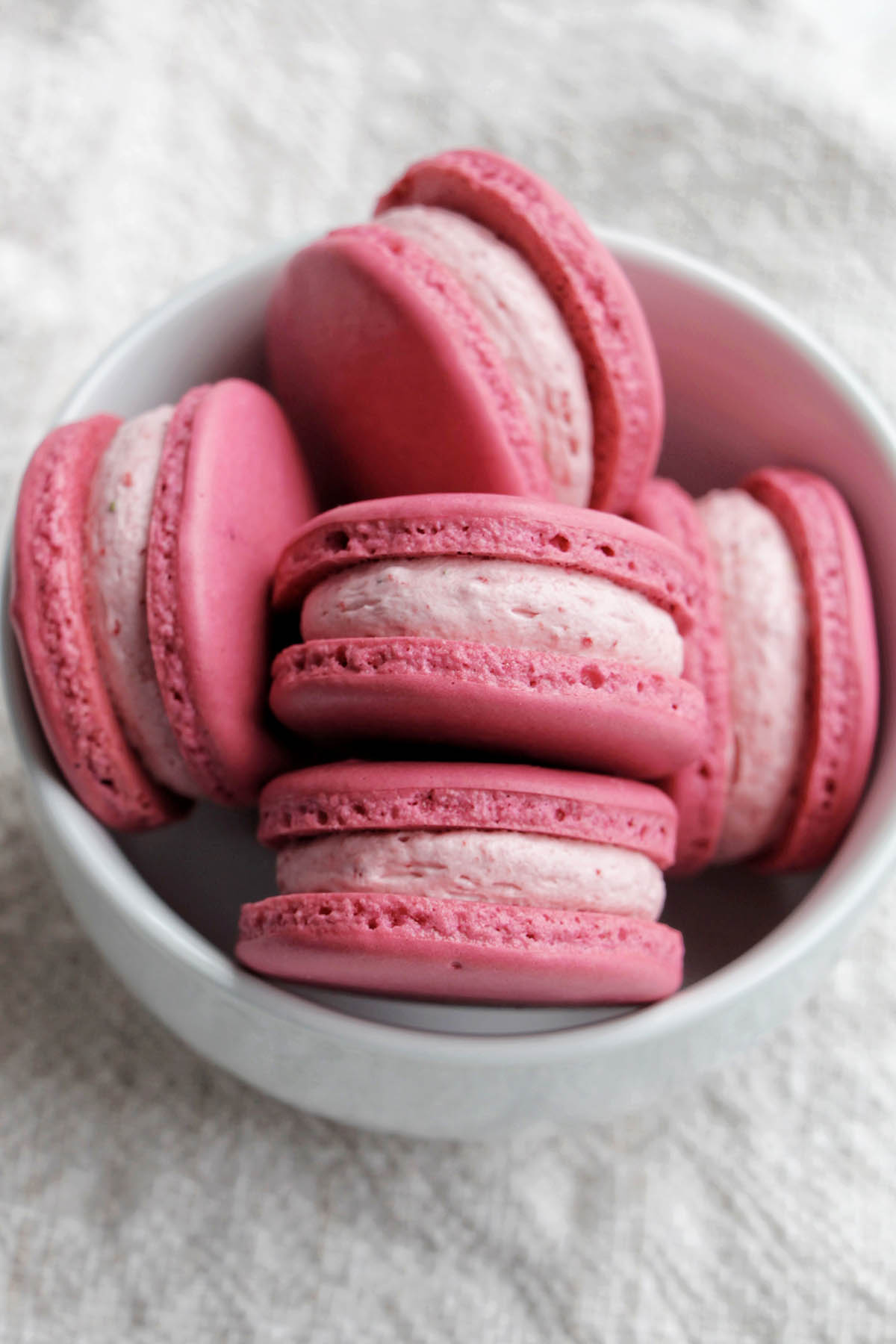 Pink macarons with strawberry cream macaron filling in a bowl.