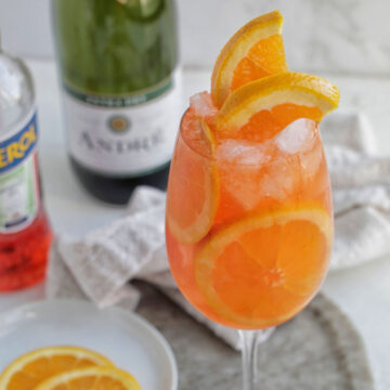 Aperol spritz cocktail in a wine glass with orange garnish.