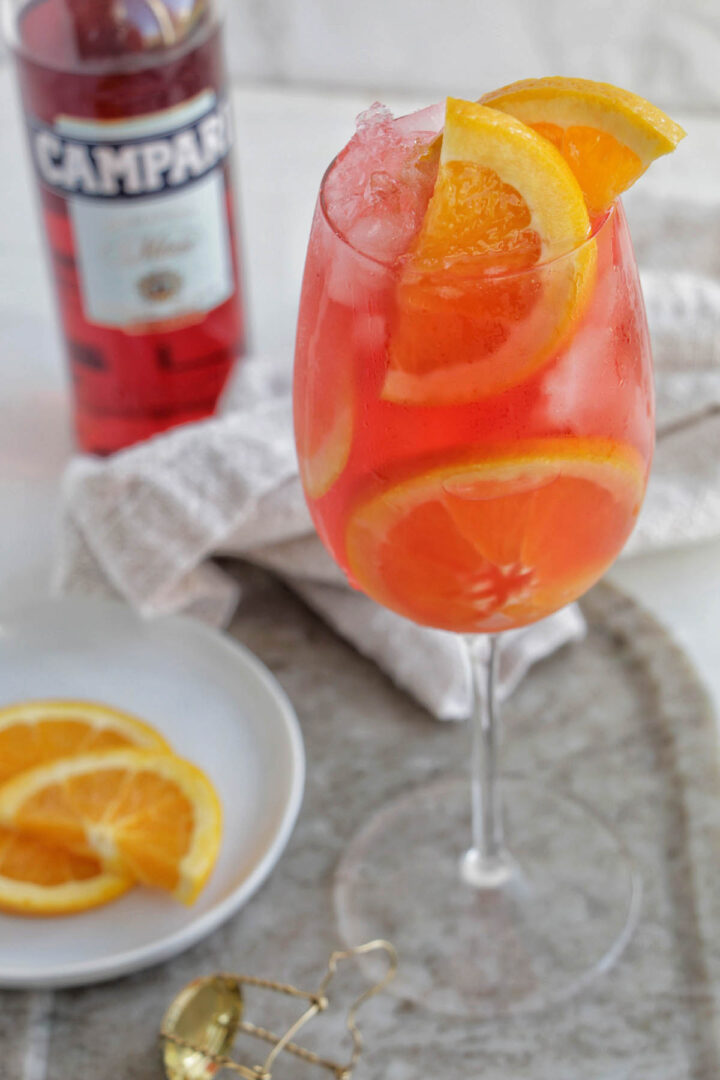 campari spritz cocktail in a wine glass with orange garnish.