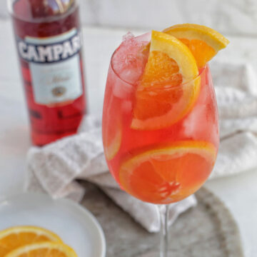 campari spritz cocktail in a wine glass with orange garnish.