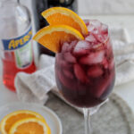 Lambrusco spritz cocktail in a wine glass with orange garnish.