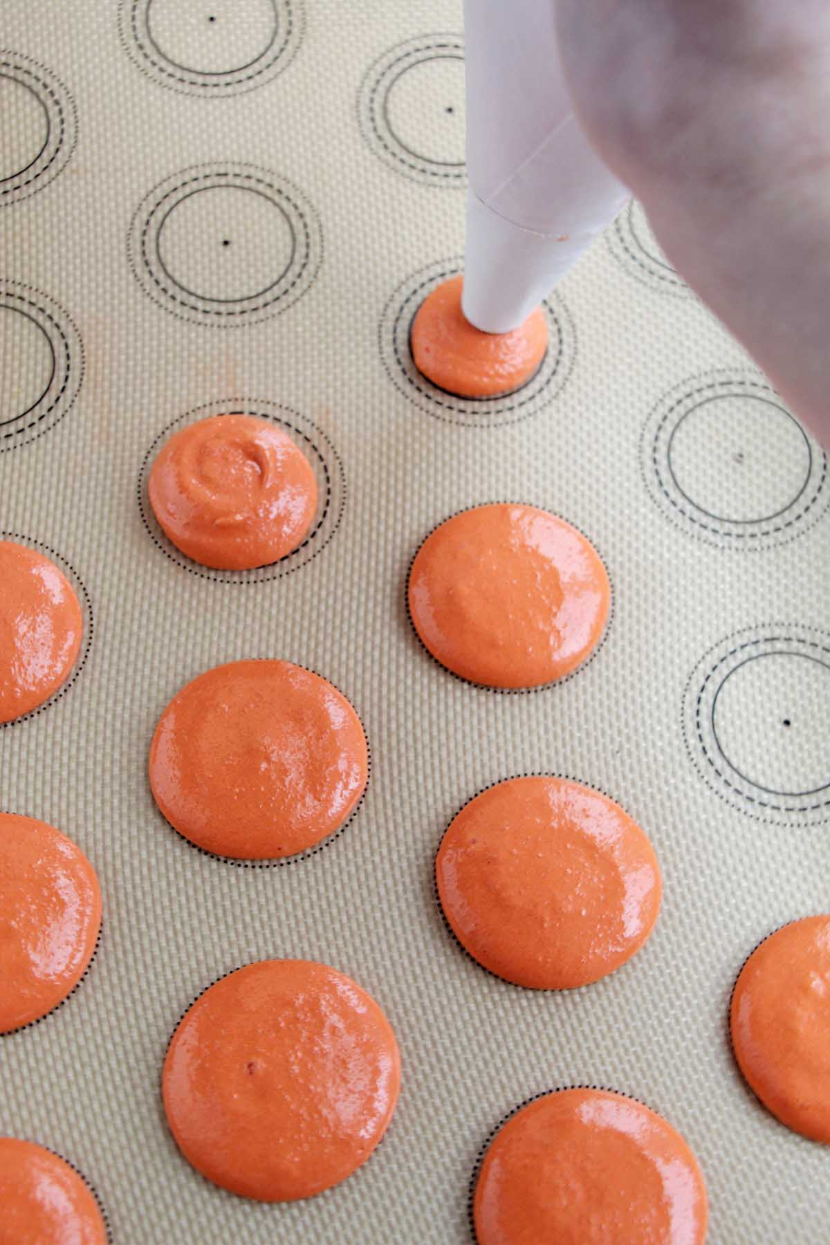 piping orange macaron batter onto a silicone baking mat.