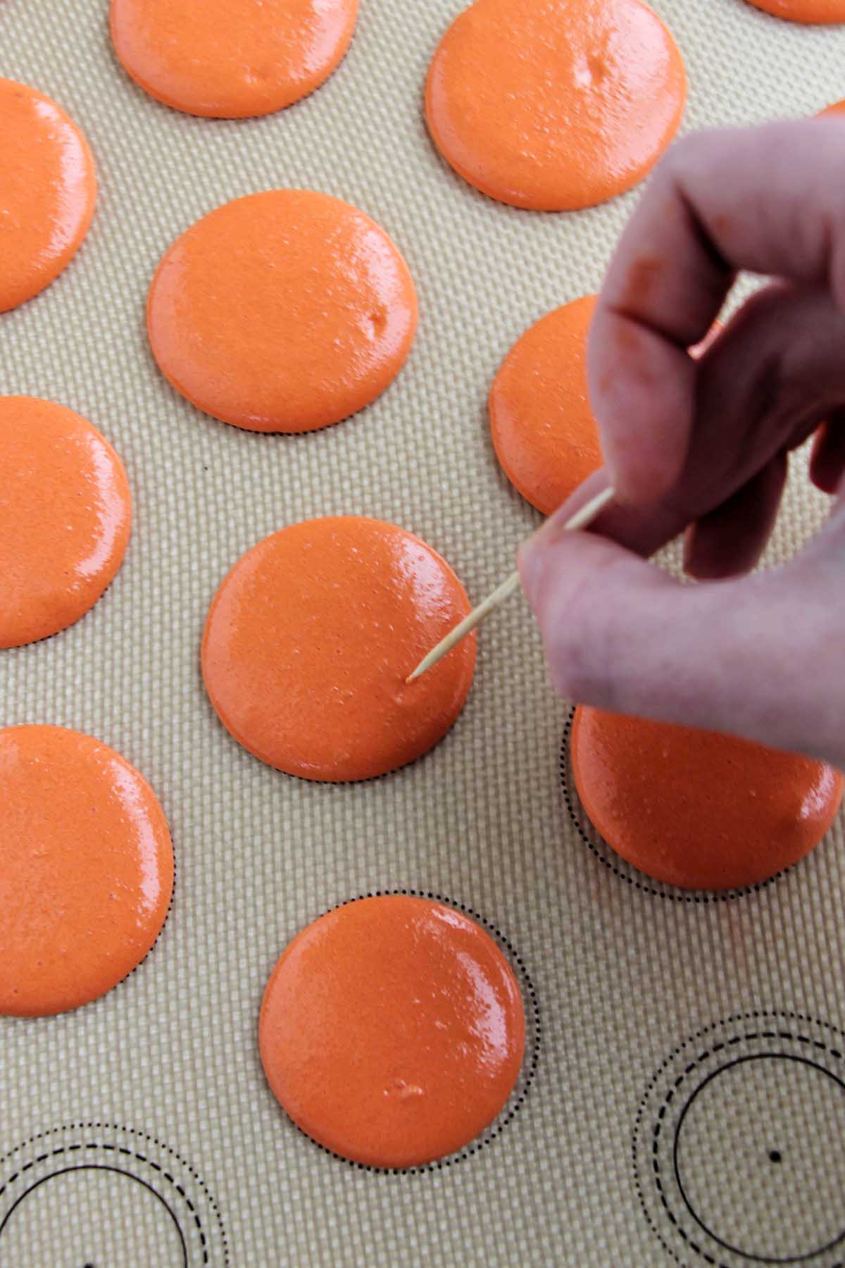 popping air bubbles in macarons with a toothpick.