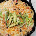 baked mexican quinoa casserole garnished with green onions and avocado.
