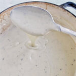 béchamel sauce dripping off a spoon into a pot.