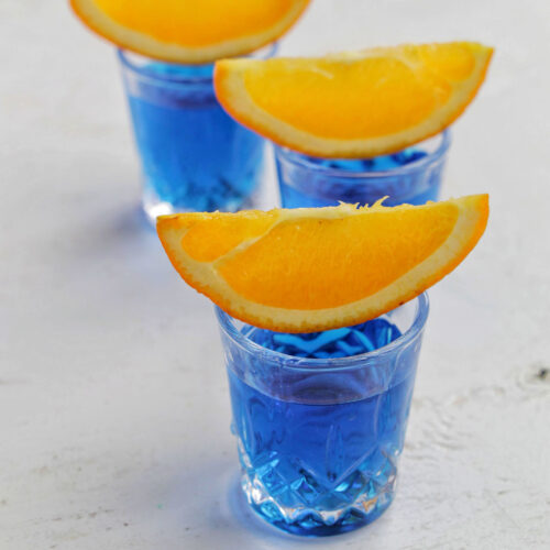 three blue shots garnished with an orange.