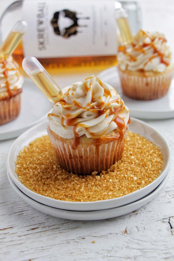 three peanut butter whiskey cupcakes next to Skrewball alcohol bottle.
