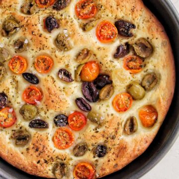 circular focaccia bread topped with olives and tomatoes.
