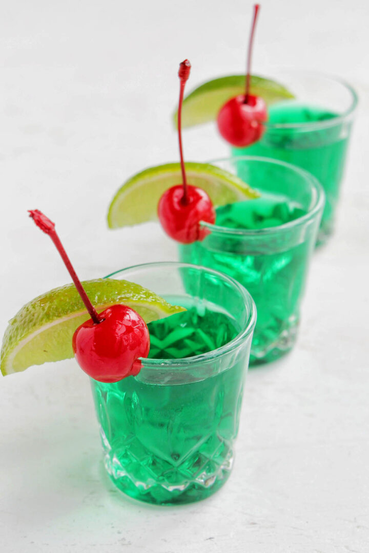 three green shots garnished with a lime and cherry.