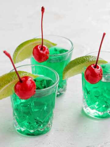 three green shots garnished with a lime and cherry.