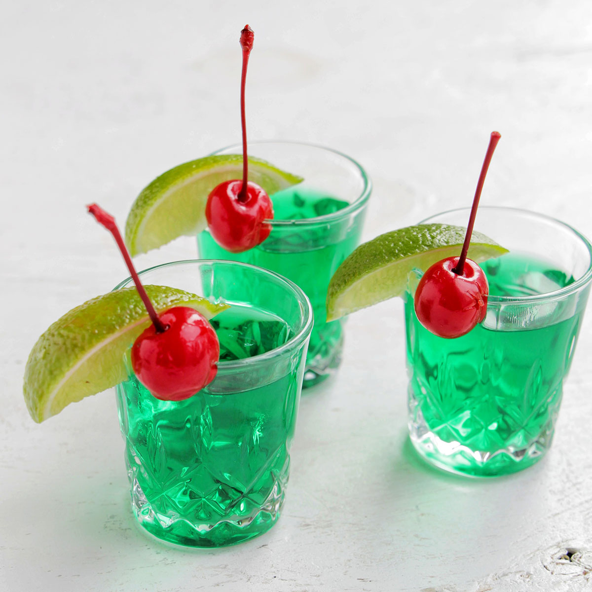 three green shots garnished with a lime and cherry.