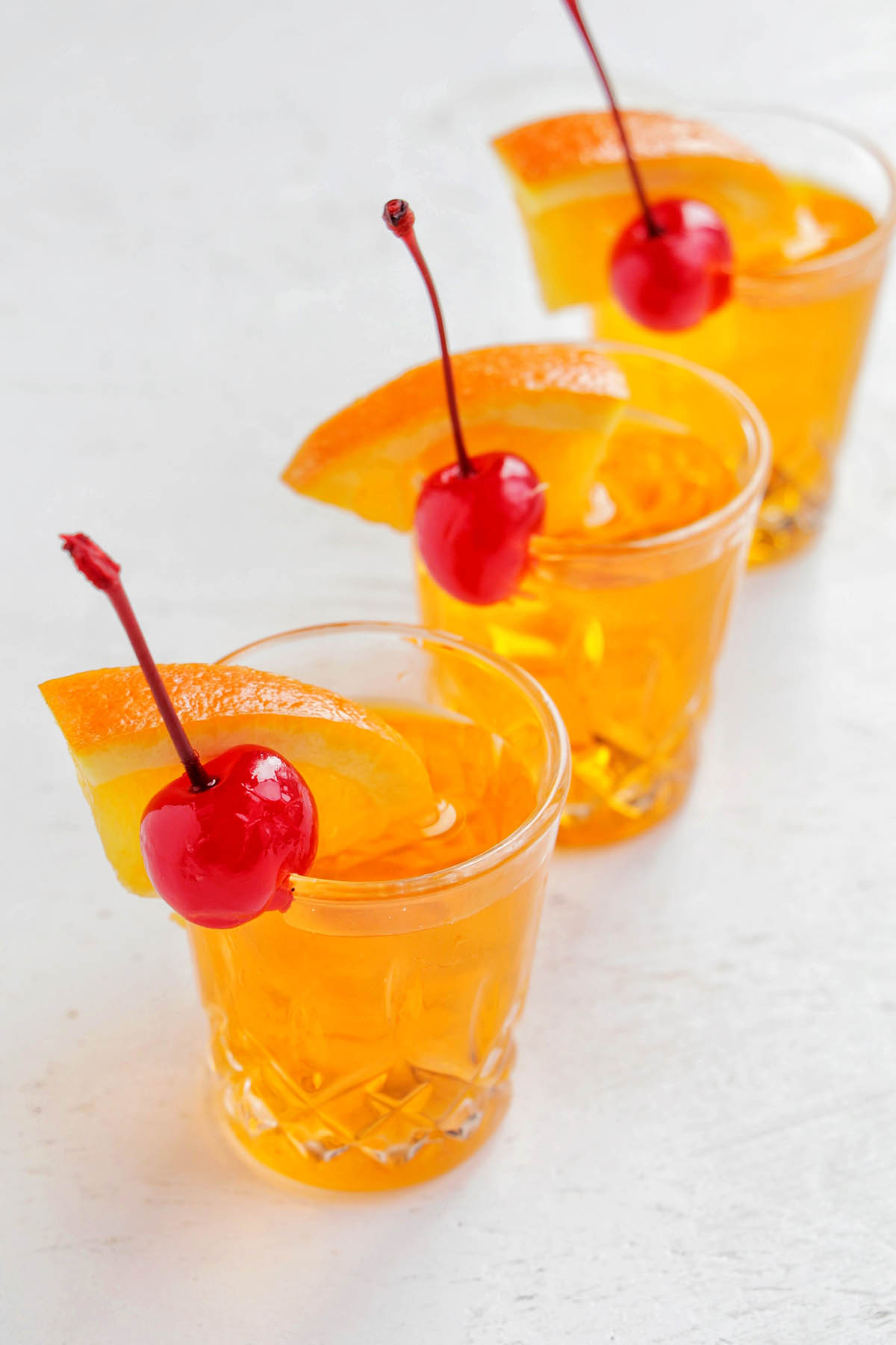 three orange shots garnished with orange and cherry.