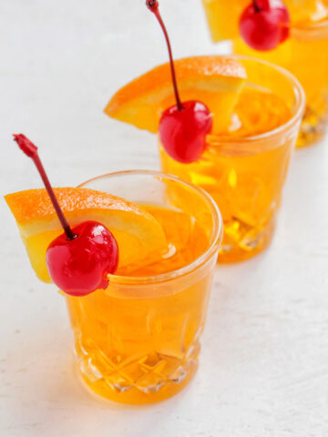 three orange shots garnished with orange and cherry.