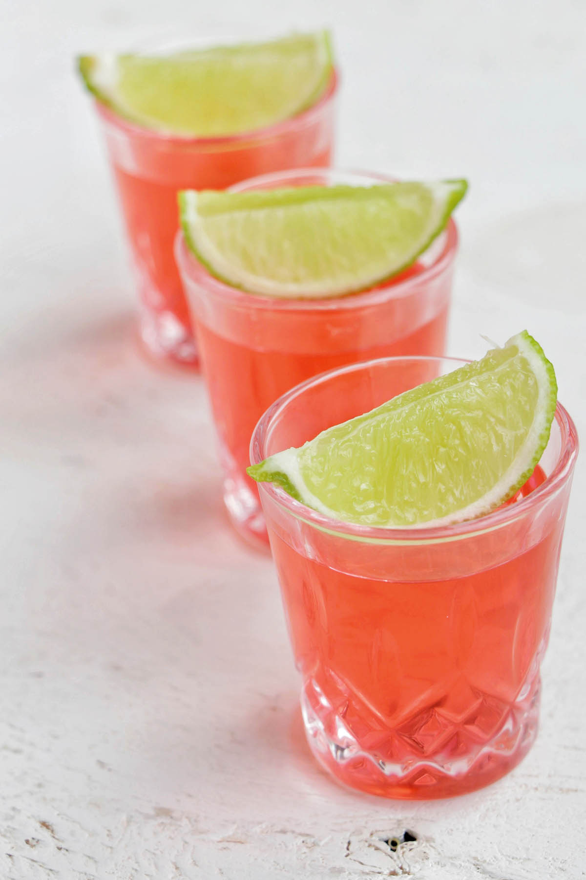 three pink shots garnished with a lime.
