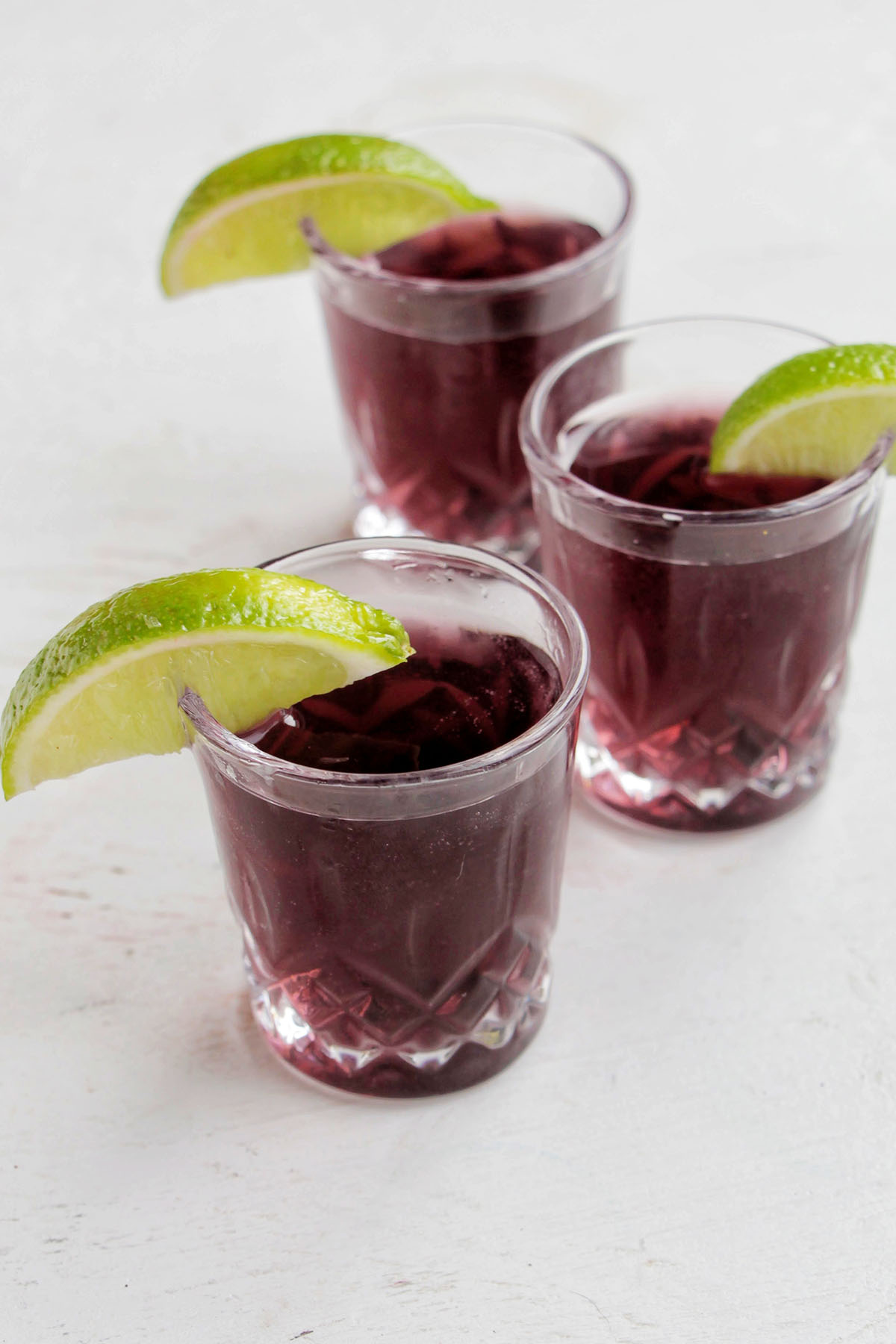three purple shots garnished with a lime.