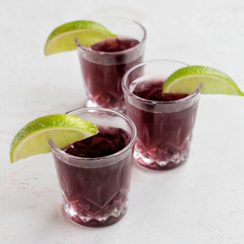 three purple shots garnished with a lime.