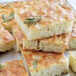 stacked rosemary focaccia bread on sheet tray.