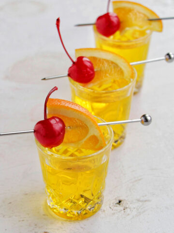 three yellow shots garnished with an orange and cherry.