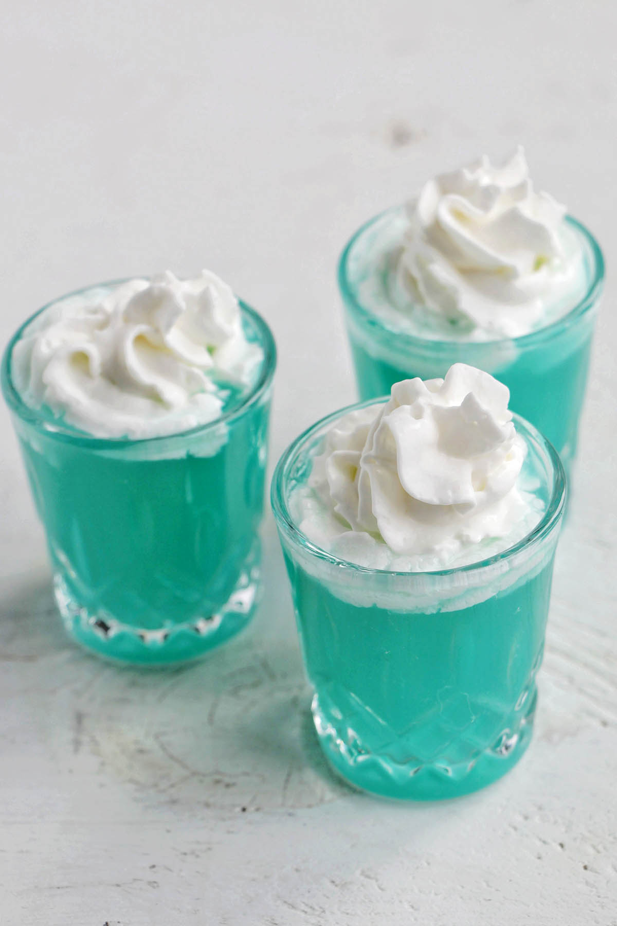three blue creamsicle shots with whipped cream.