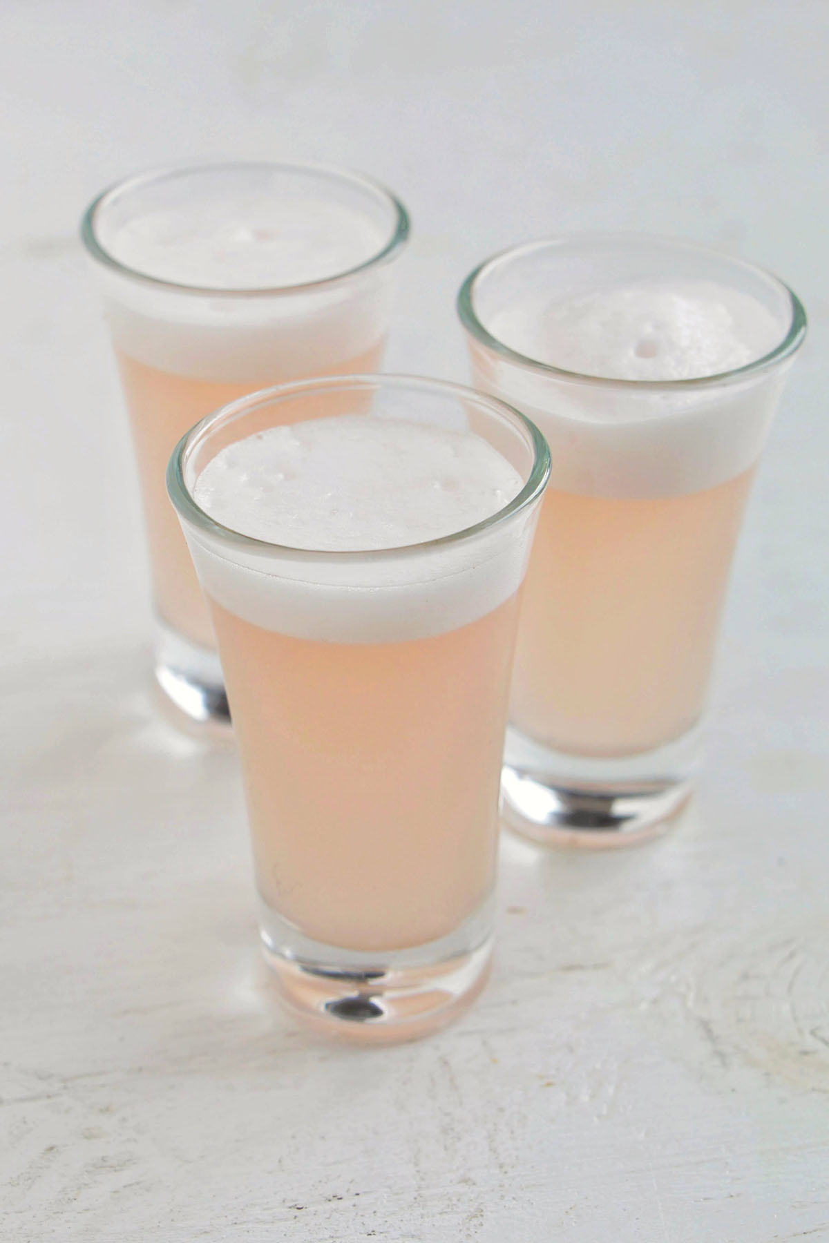 three hibiscus sour shots with egg white tops.