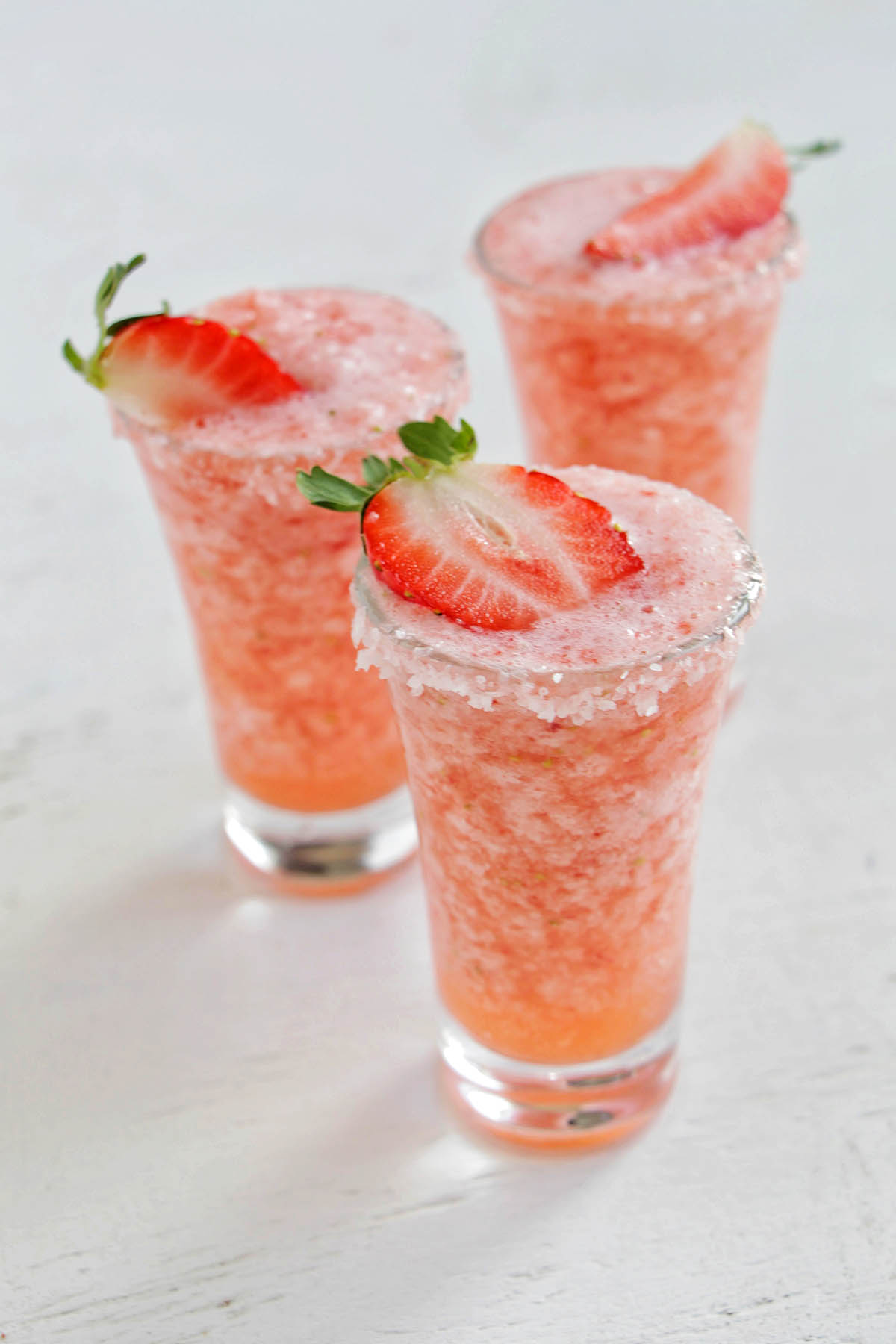 Frozen strawberry margarita shots garnished with strawberry.
