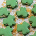 shamrock macarons laying on gold sprinkles.