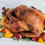 roasted turkey on serving platter with fruit and herbs.