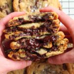 hands holding hot fudge filled chocolate chip cookies.