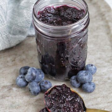 blueberry jam in a jar next to a spoonful of jam.