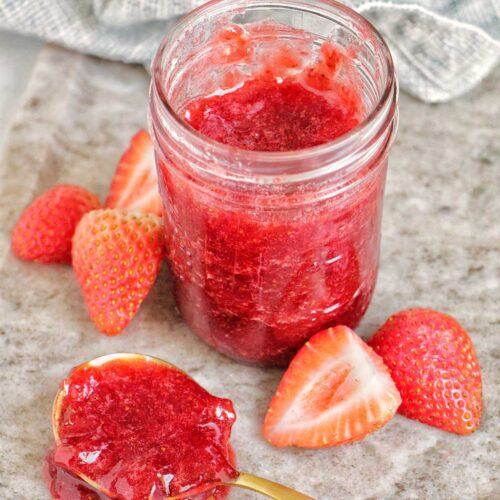 strawberry jam in a jar next to a spoonful of jam.