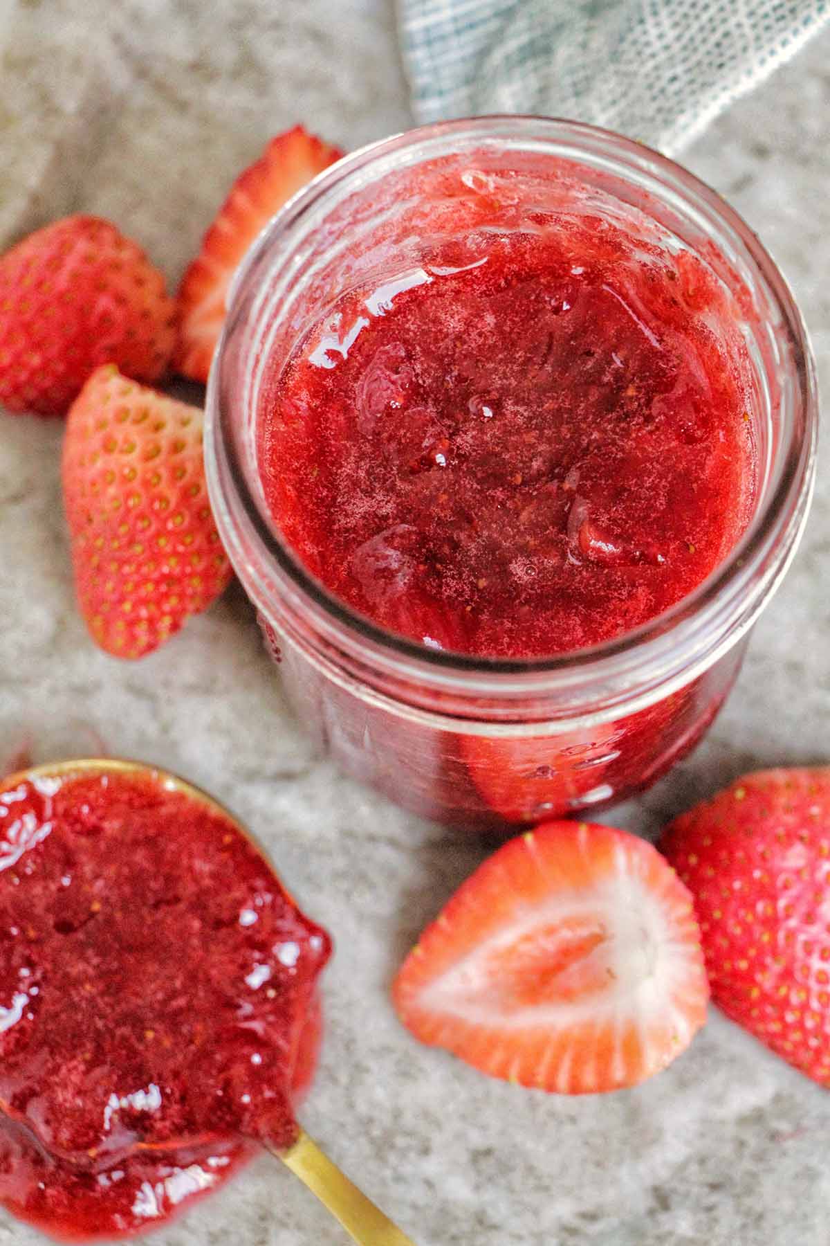 strawberry jam in a jar next to a spoonful of jam.