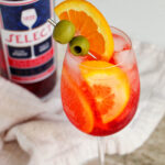 Select spritz in wine glass next to liquor bottle.