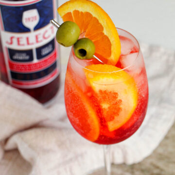 Select spritz in wine glass next to liquor bottle.