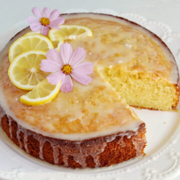 lemon olive oil cake topped with glaze, lemons, and edible flowers.