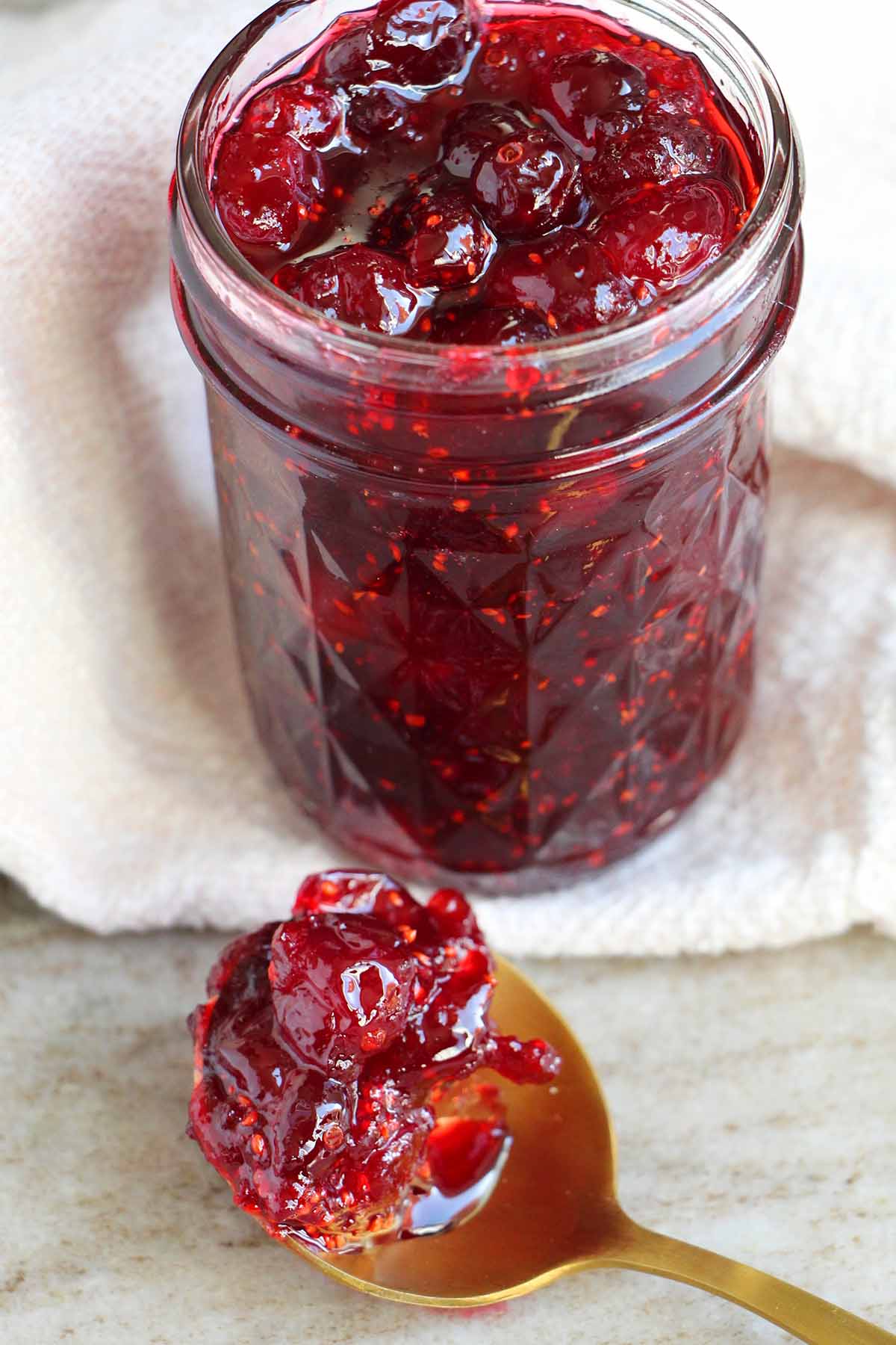 cranberry jam in a mason jar with a spoon holding jam.