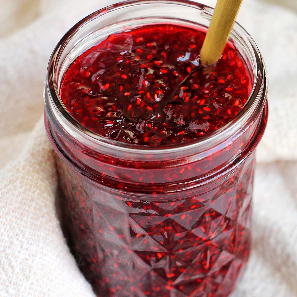 raspberry jam in a mason jar with a spoon.