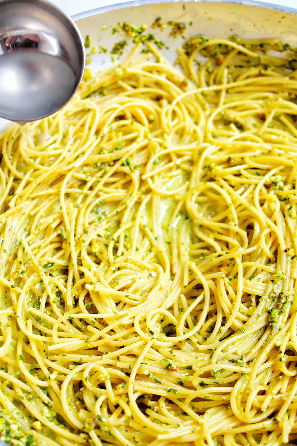 adding pasta water to pesto pasta.